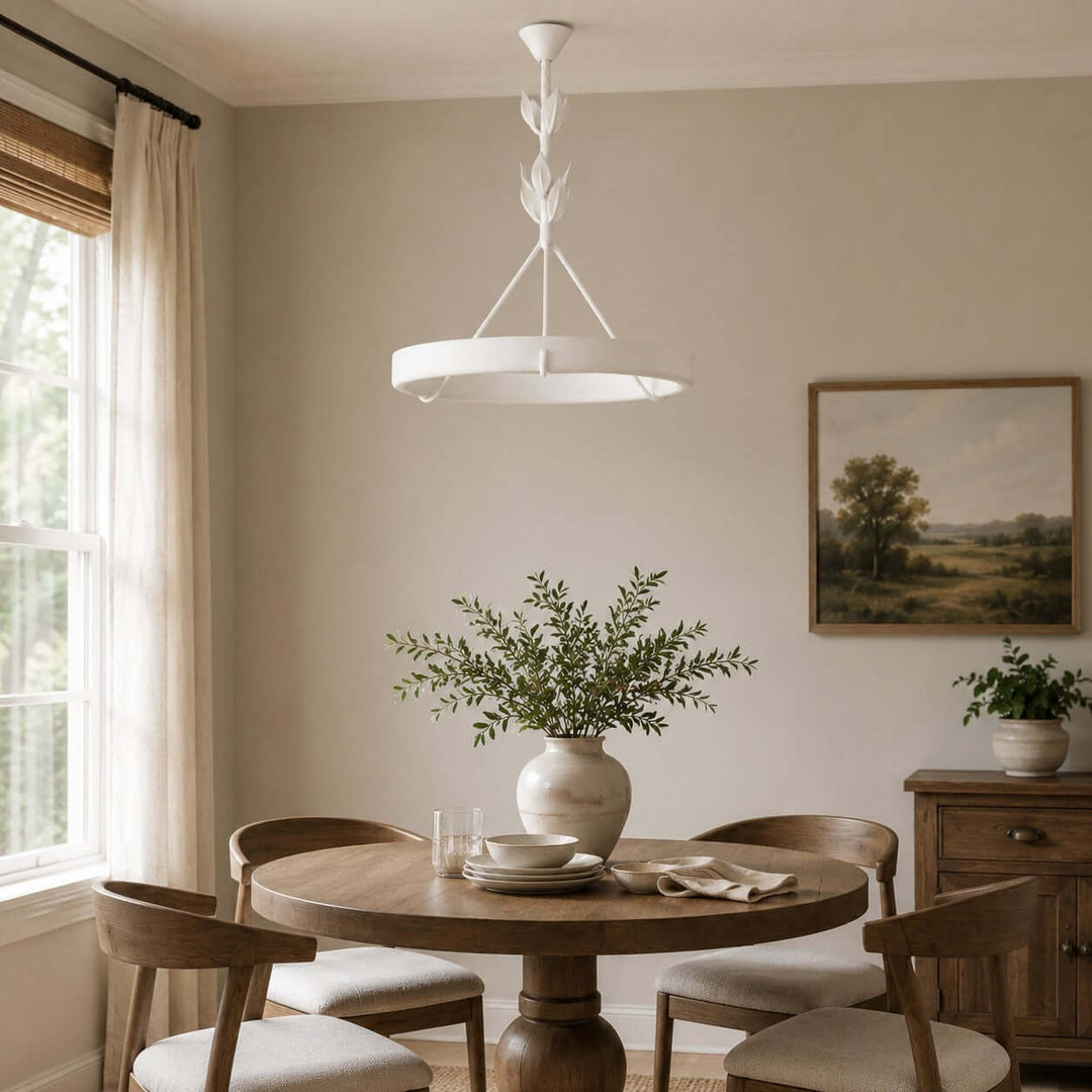White Tinsley dining room chandelier above a round wood table beside a sunlit window.
