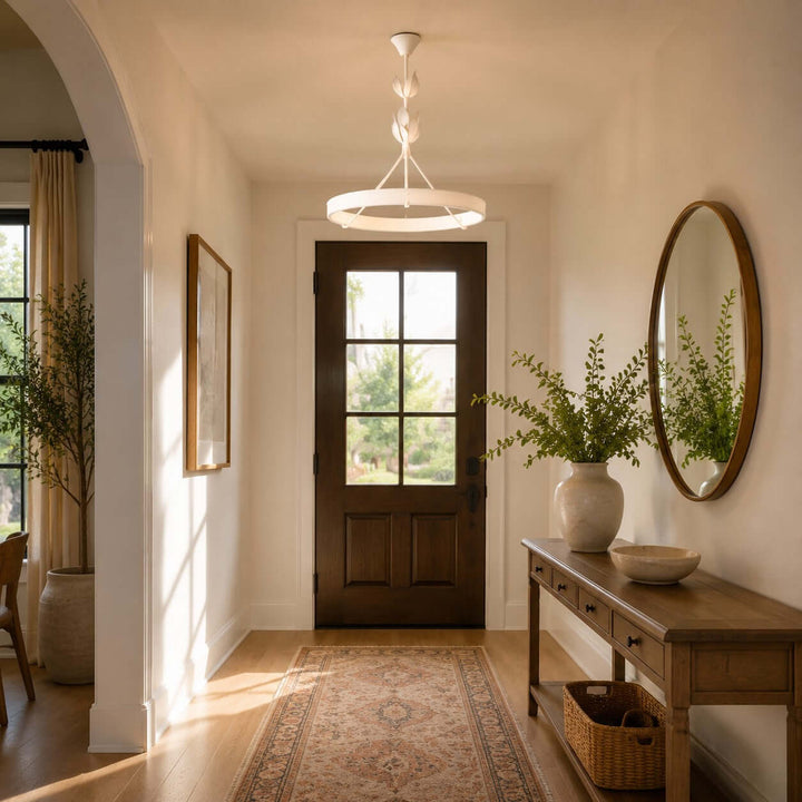 White ring chandelier lighting a warm entryway with a wood console, round mirror, and front door.