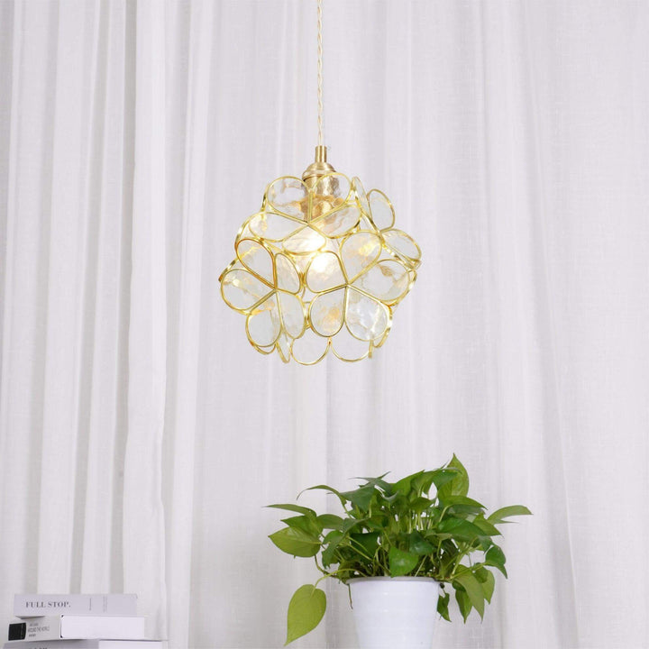 Transparent glass petal pendant light displayed above a green plant against white curtains