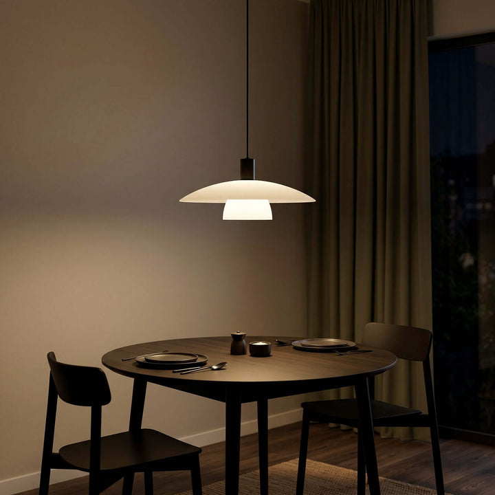Glowing Verona pendant light above a dark round dining table set for two at night