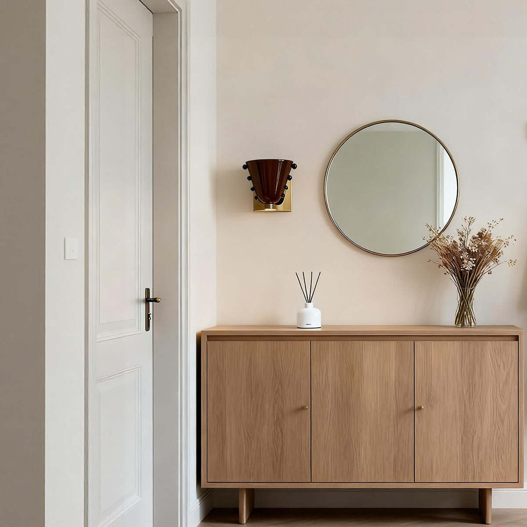 Brown Vestra wall sconce beside a round mirror over a wood entryway console