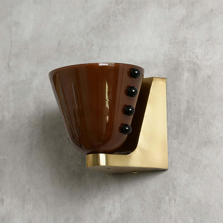 Side view of a brown Vestra glass wall sconce with black accents and a gold backplate