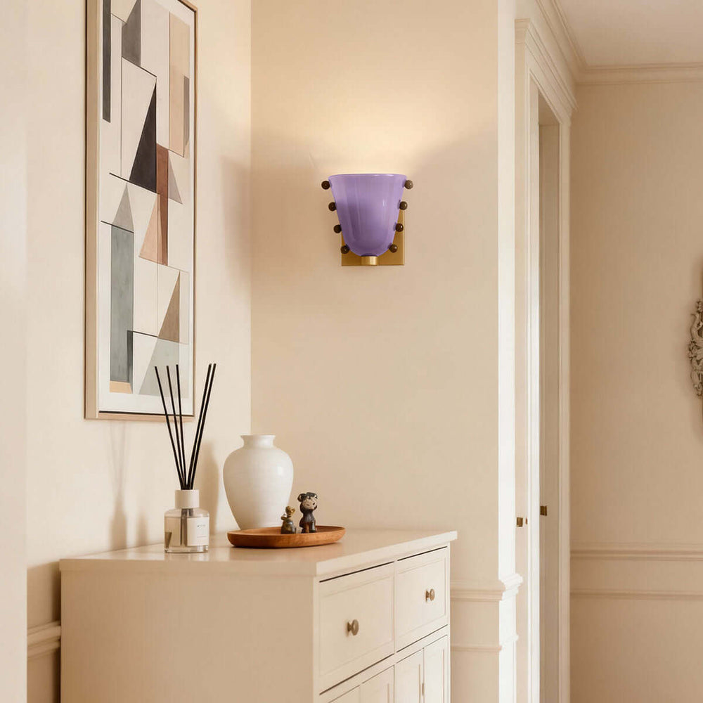 Purple Vestra glass wall sconce above a white entryway cabinet and geometric artwork