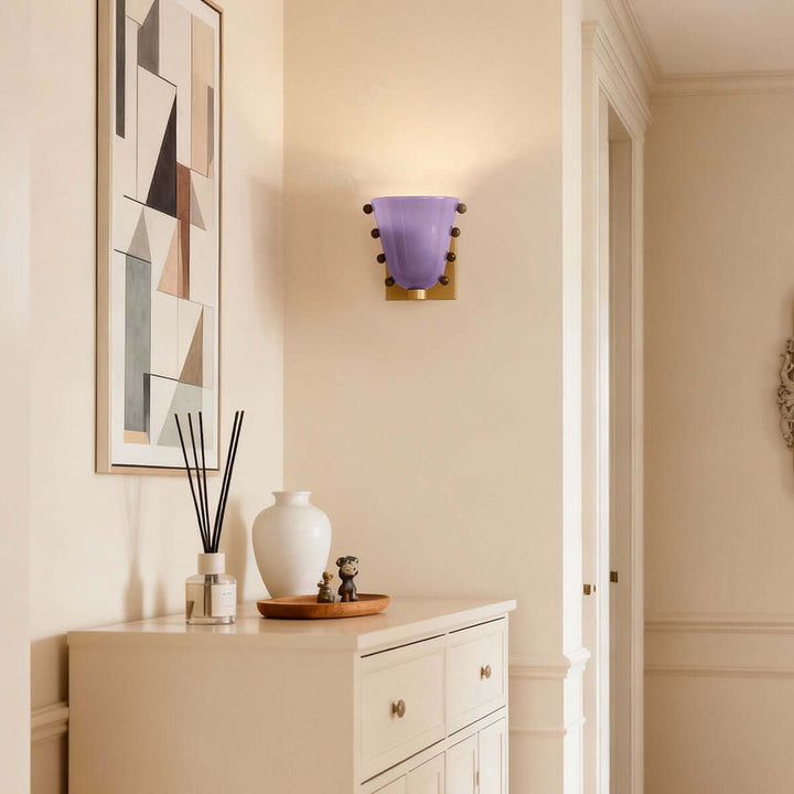 Purple Vestra glass wall sconce above a white entryway cabinet and geometric artwork