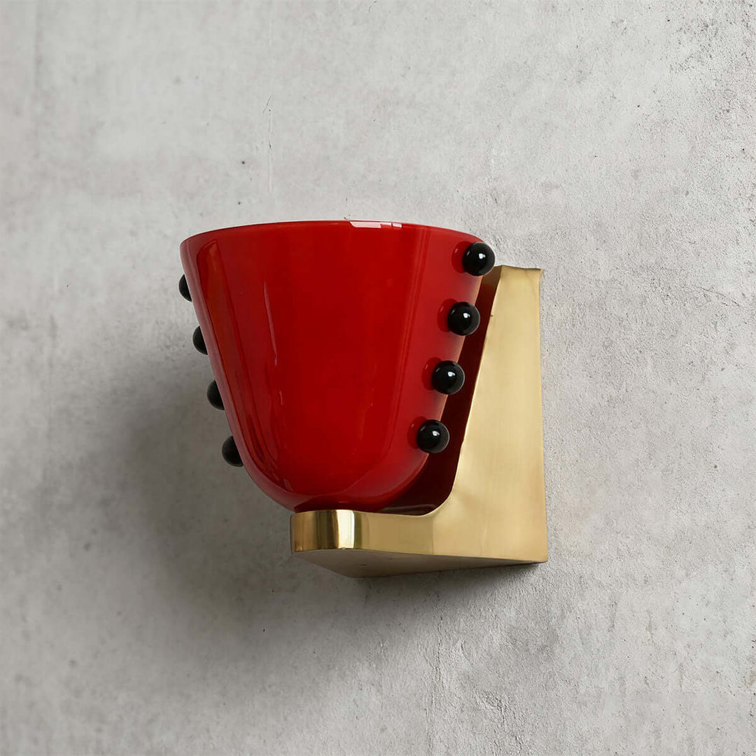 Side view of a red Vestra glass wall sconce with black accents and a gold backplate