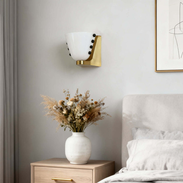White Vestra glass wall sconce mounted above a wood nightstand with dried flowers