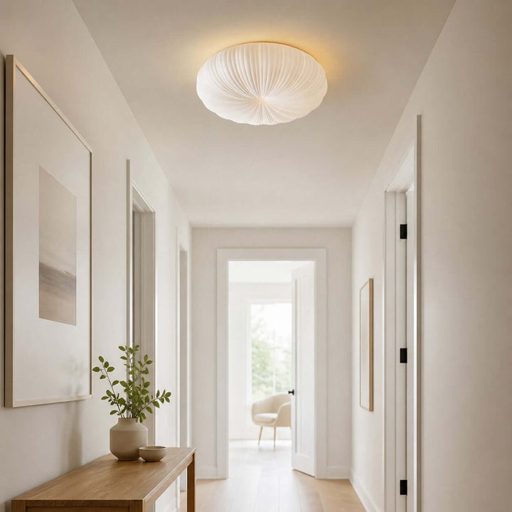 White pleated ceiling light mounted in a clean hallway near a doorway.