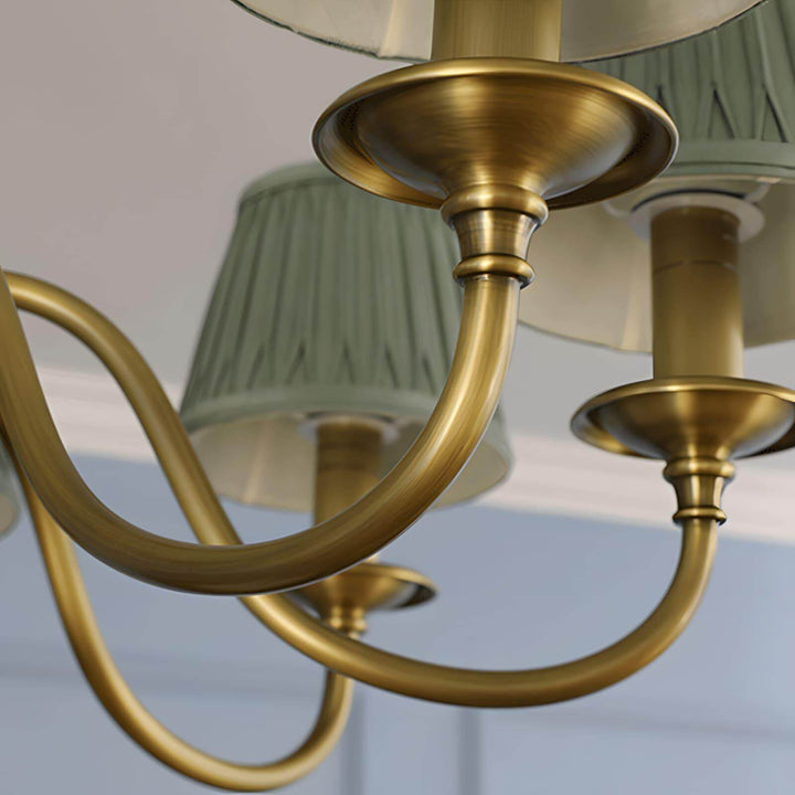 Close-up of a curved brass chandelier arm and shade support.