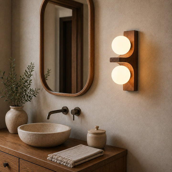 Wood double wall sconce beside a round mirror above a bathroom vanity.