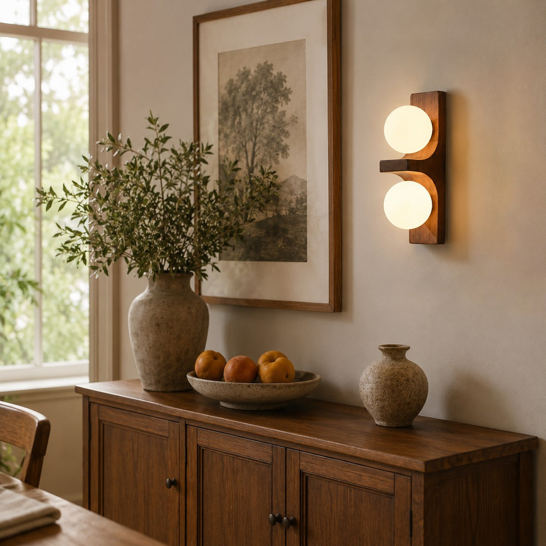 Wood double wall sconce glowing above a cabinet with framed art and decor.