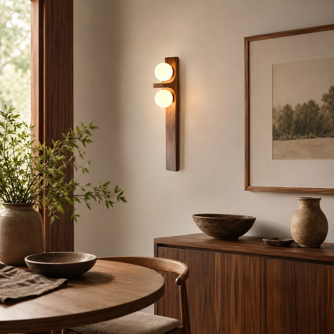 Tall wood double wall sconce glowing above an entry table with a bowl and plant.