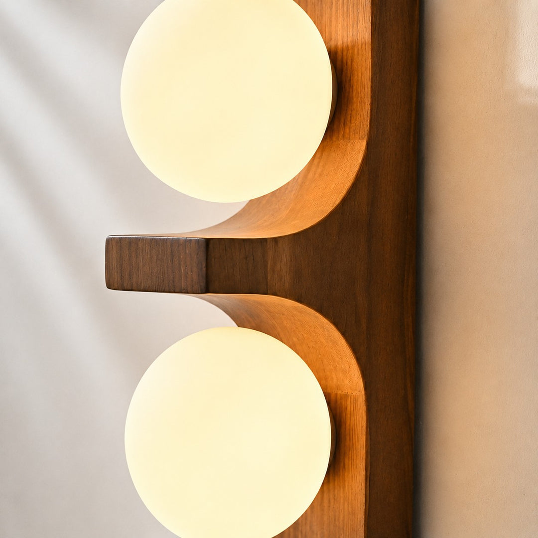 Close-up of two glowing white glass globes and curved wood supports.