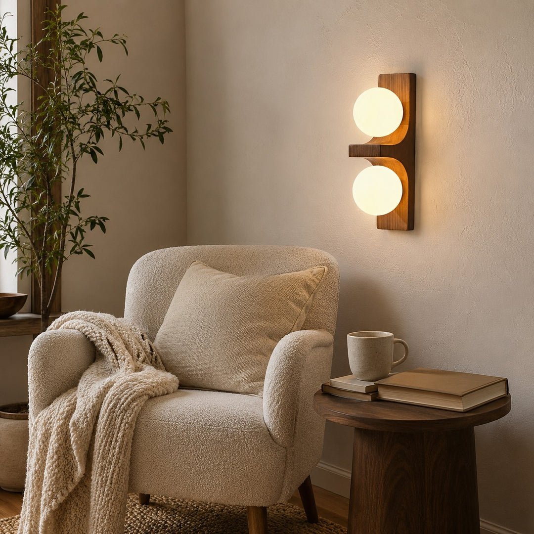 Wood double wall sconce glowing beside an armchair and small side table.