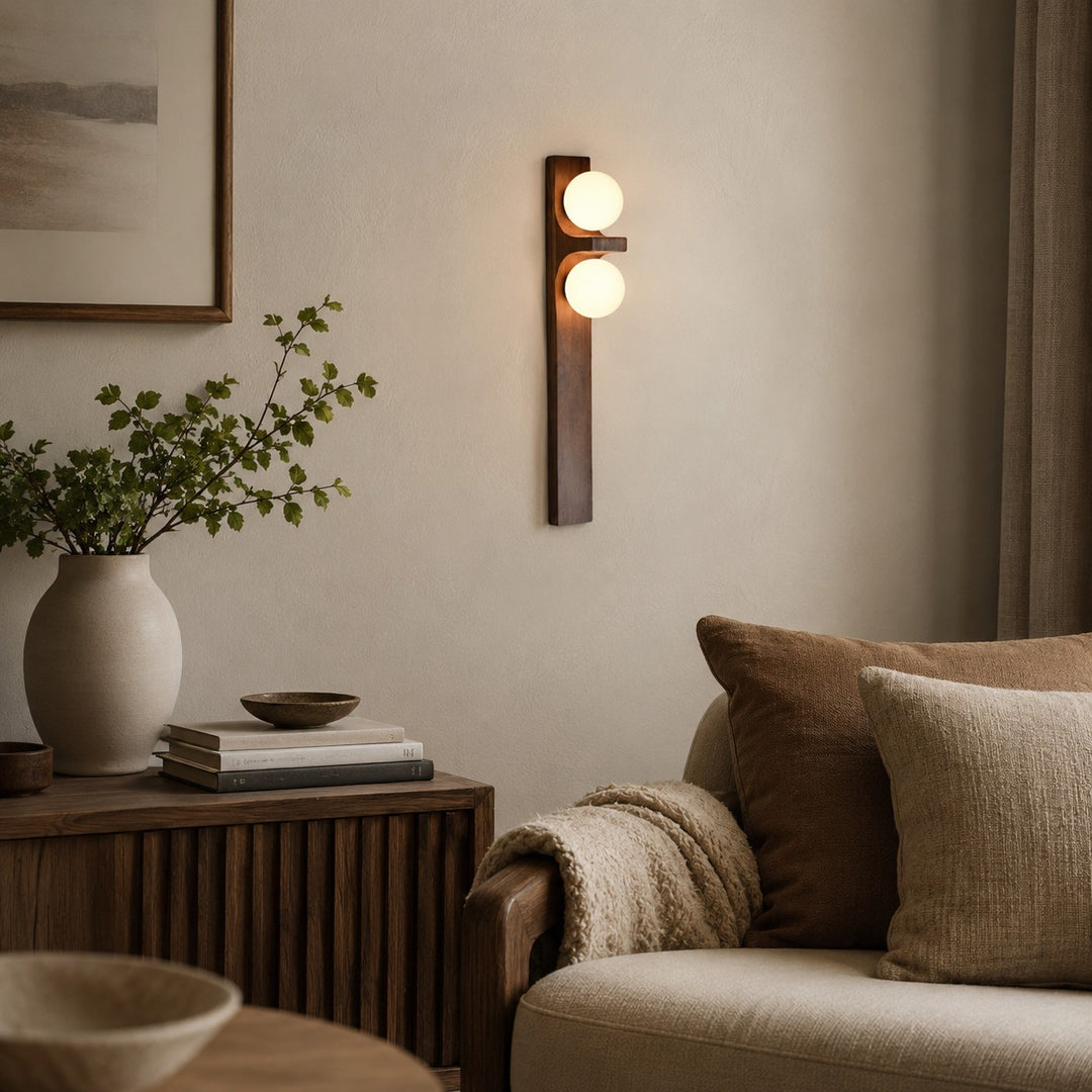 Tall wood double wall sconce mounted beside a sofa and small cabinet.