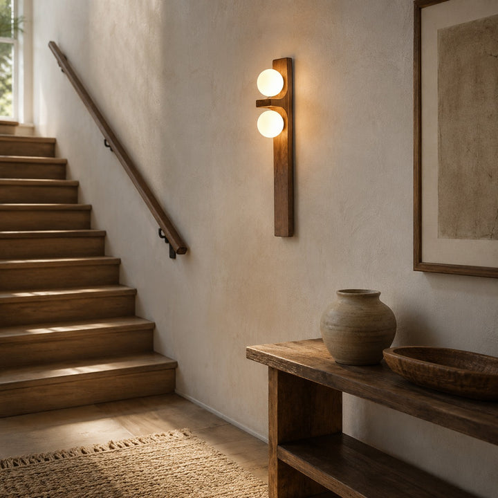 Double wall sconce glowing near a staircase above a console table.