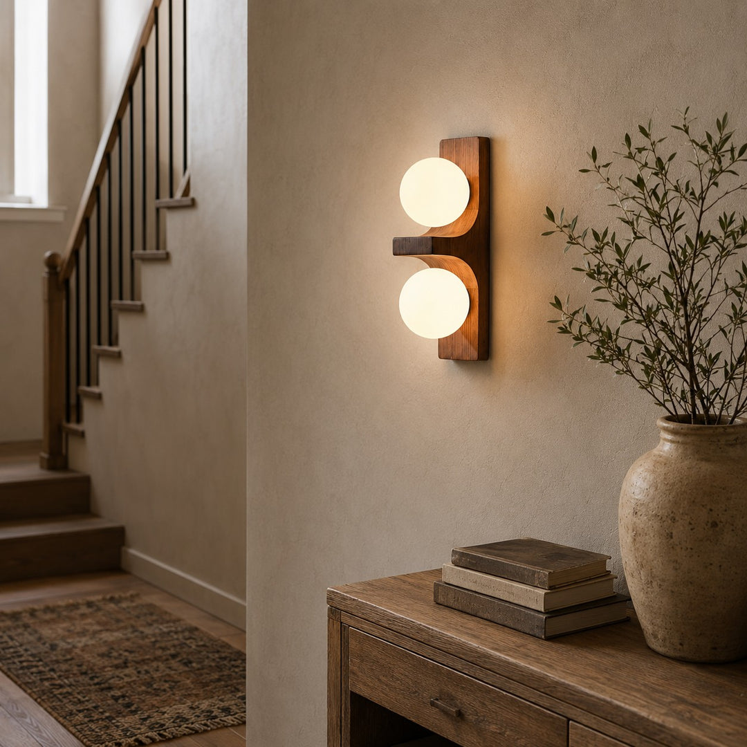 Double wall sconce glowing on a stairway wall beside a console and vase.