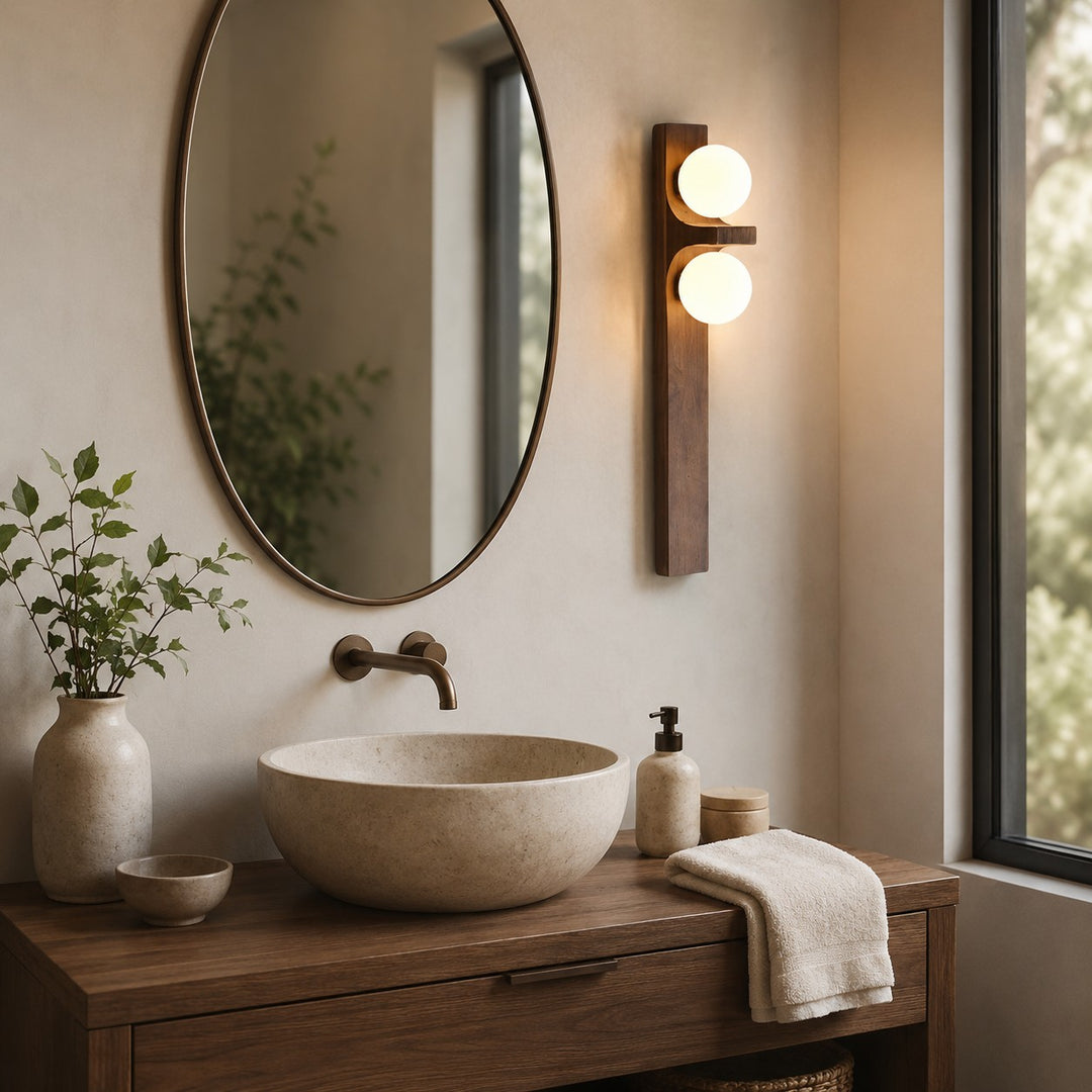 Slim wood double wall sconce beside a round mirror and vessel sink.