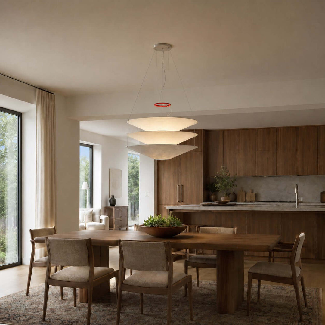 Layered white pendant light hanging between a dining table and kitchen area.