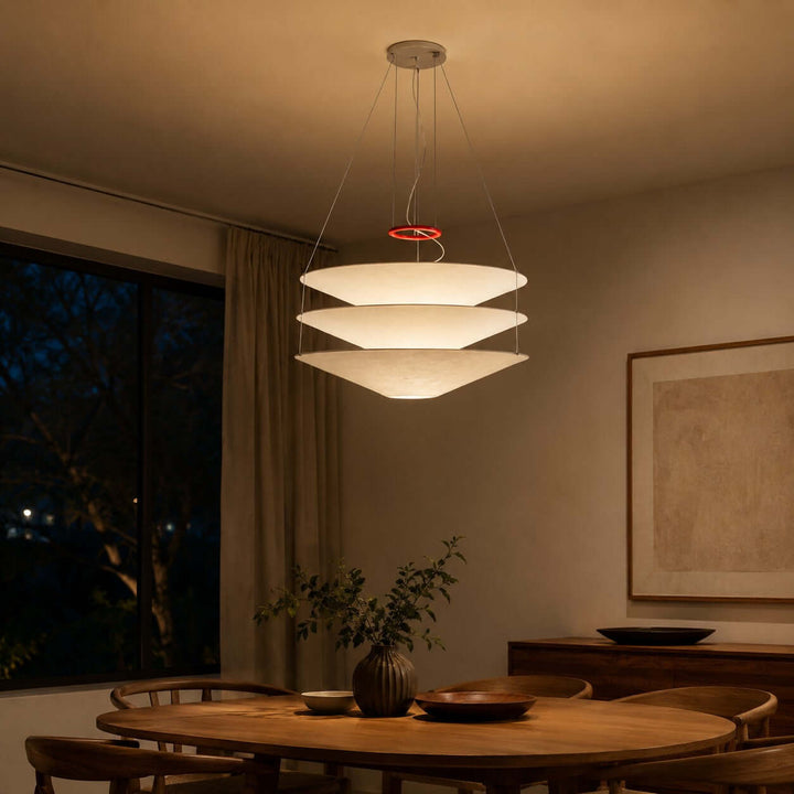 Layered pendant light glowing warmly above a dining table in the evening.