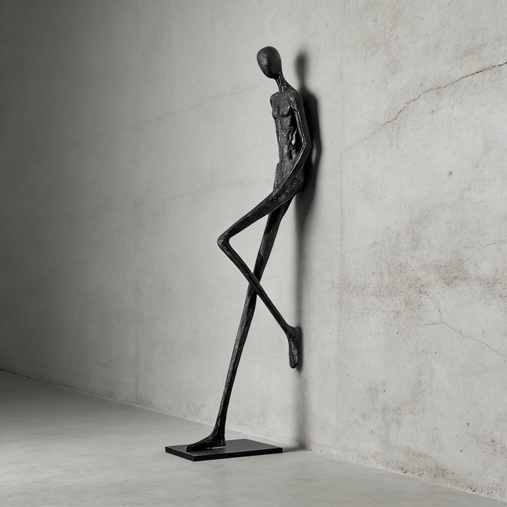 Black abstract sculpture with a slim base shown on a concrete wall.