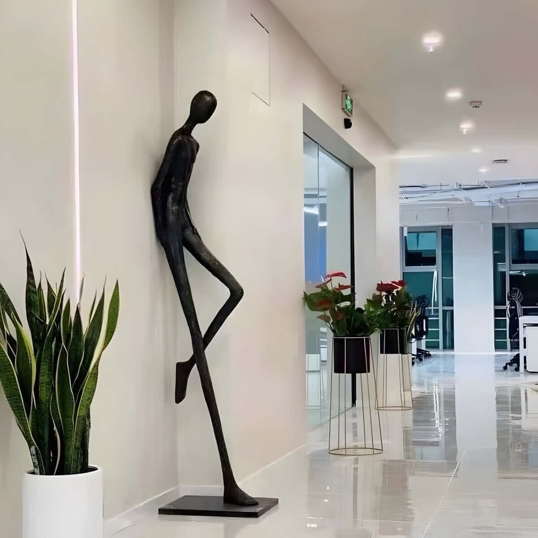 Tall black resin sculpture beside a plant in a modern lobby corridor.