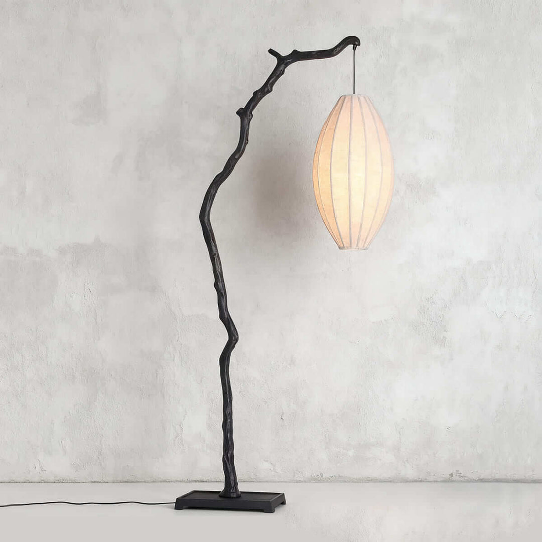 Black tree floor lamp with a pale oval fabric shade shown on a gray wall.