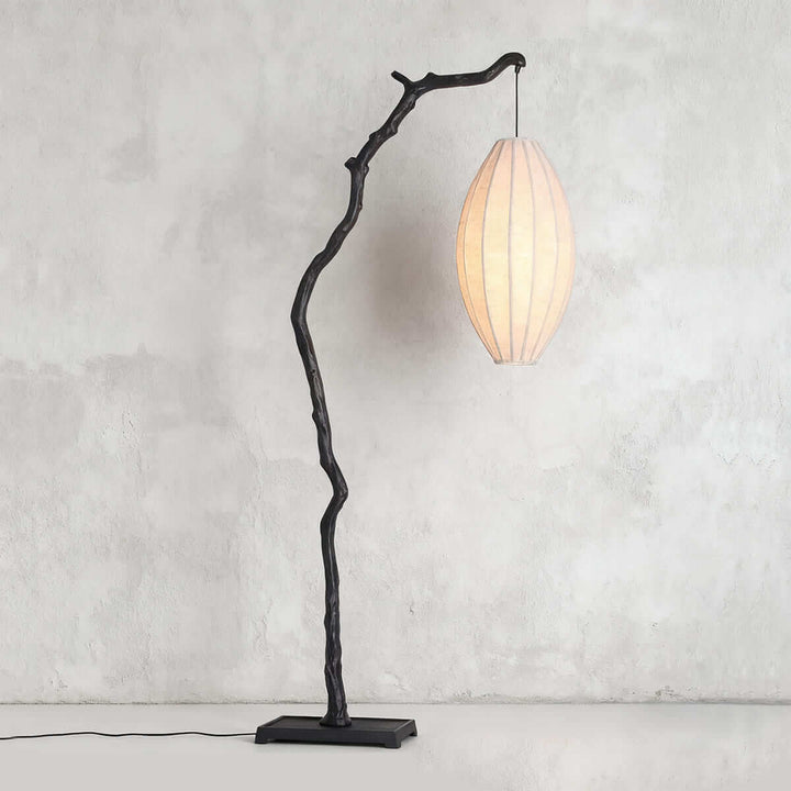 Black tree floor lamp with a pale oval fabric shade shown on a gray wall.