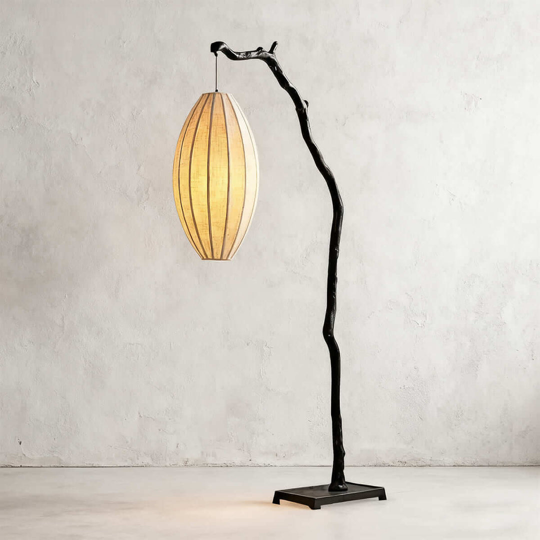 Black tree floor lamp with a glowing oval fabric shade on a gray wall background.