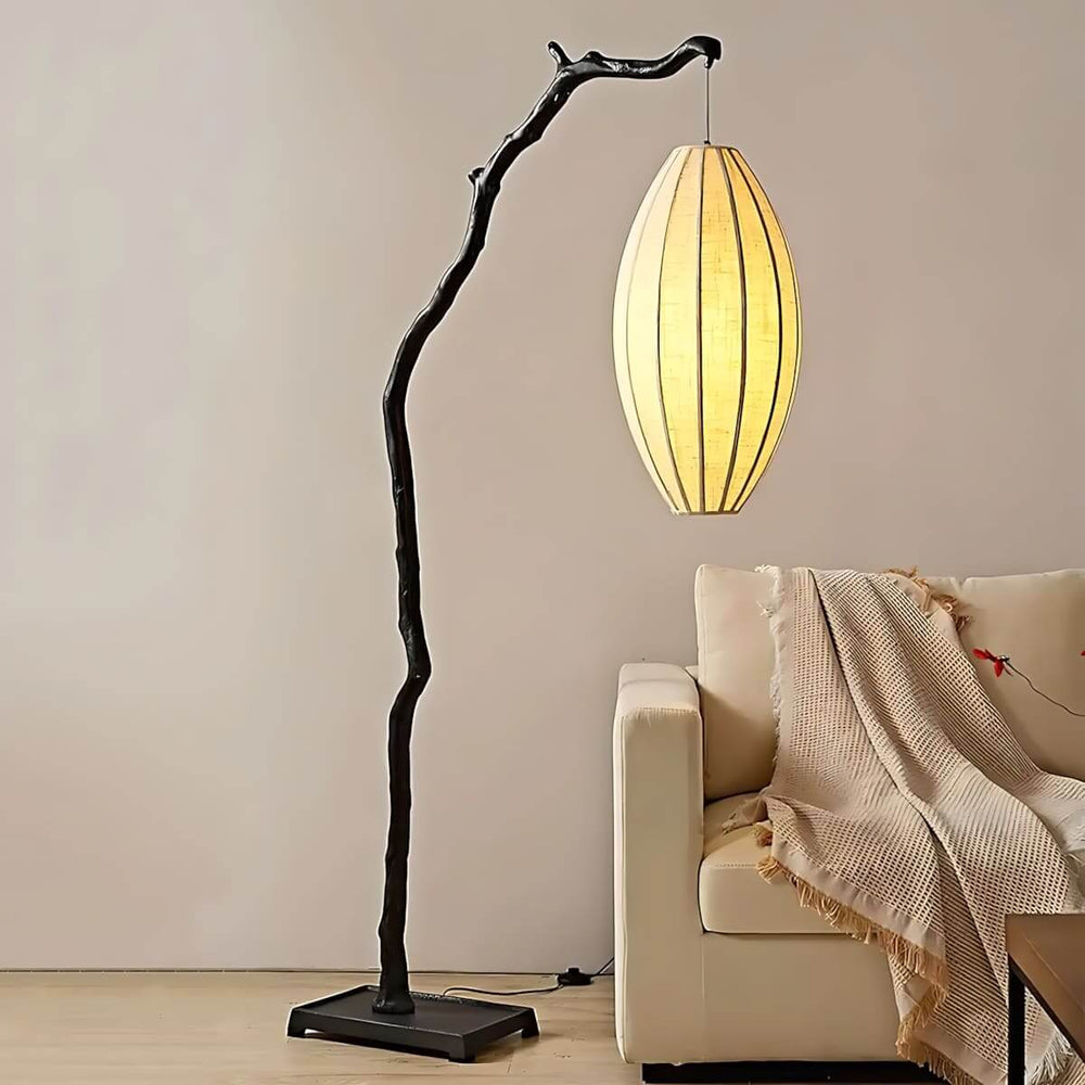 Black tree branch floor lamp with an oval fabric shade beside a light armchair.