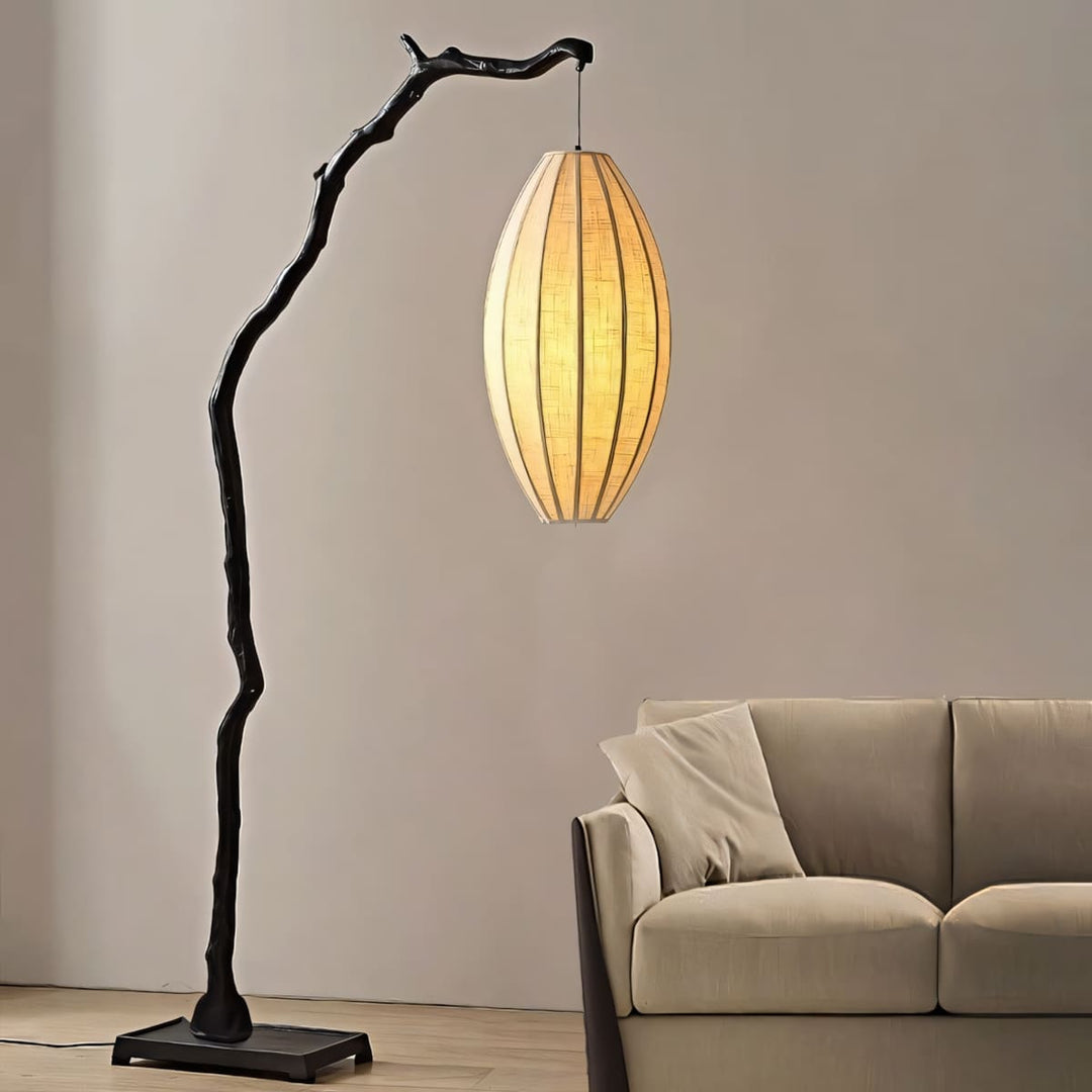 Black tree floor lamp glowing beside a neutral sofa on a clean wall.