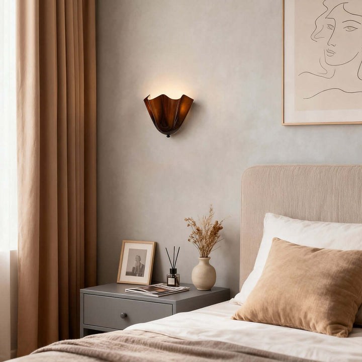 Amber glass wall sconce above a nightstand in a soft bedroom setting.