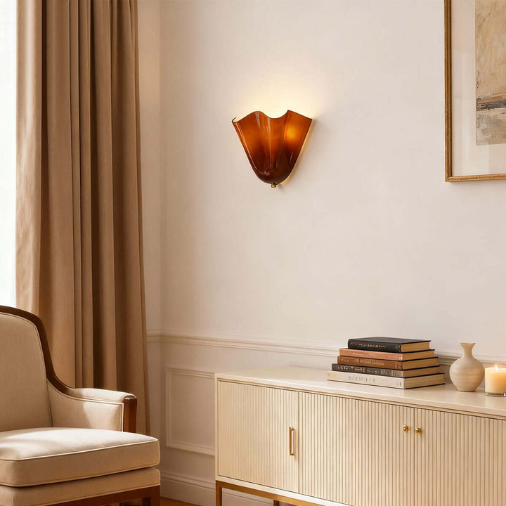 Amber glass wall sconce mounted above a low cabinet with books and decor.