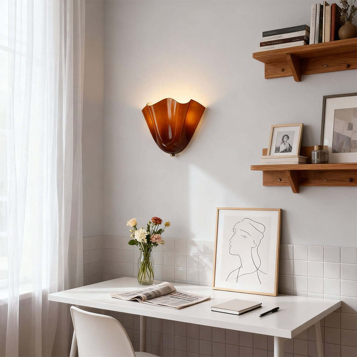 Amber glass wall sconce above a small desk with shelves and framed art.