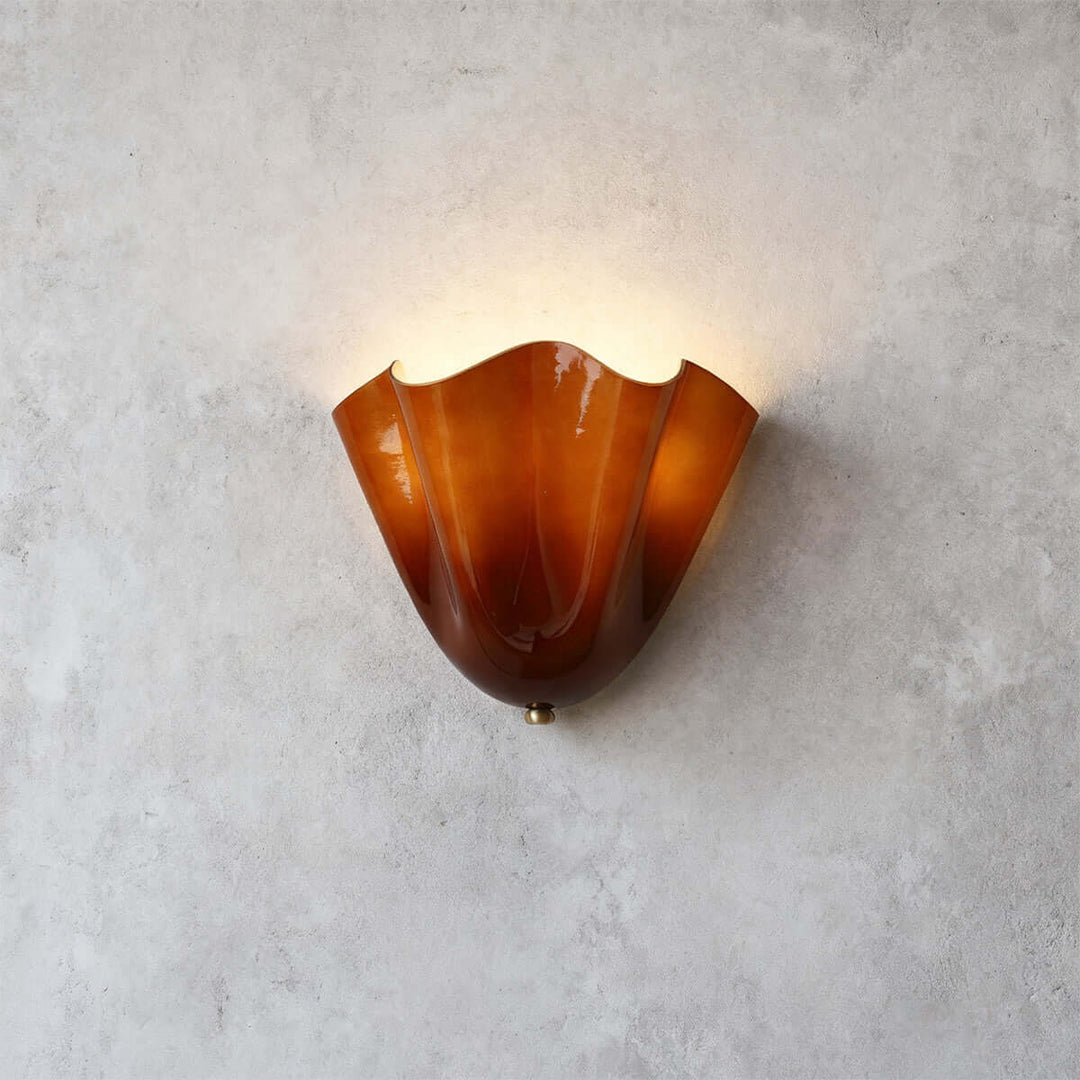 Amber glass wall sconce with gold hardware glowing on a gray wall.