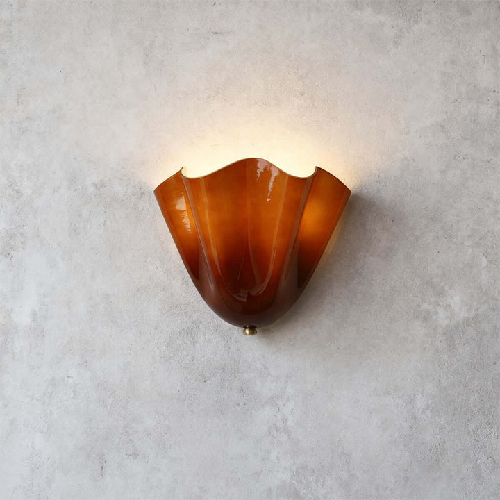 Amber glass wall sconce with gold hardware glowing on a gray wall.