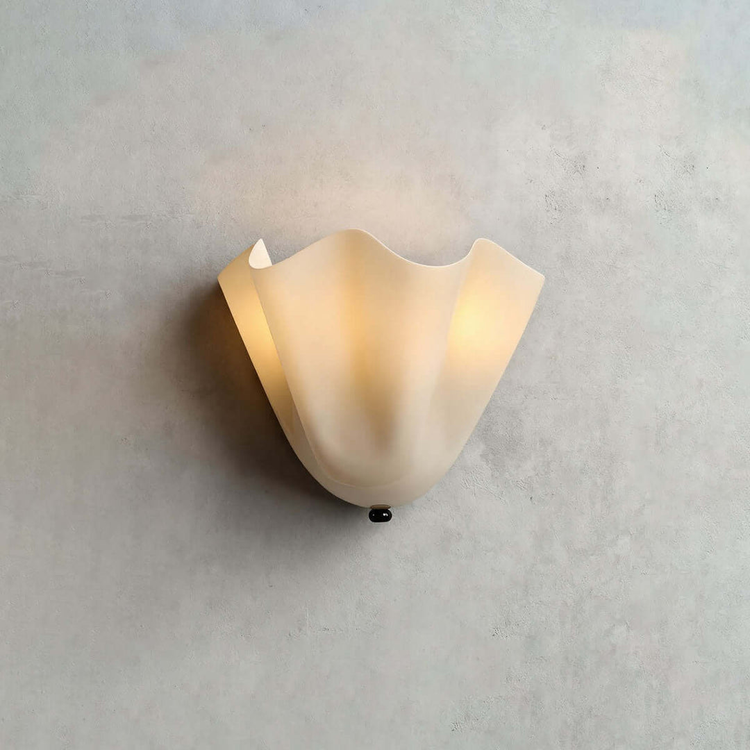 Beige glass wall sconce with black hardware glowing on a pale gray wall.