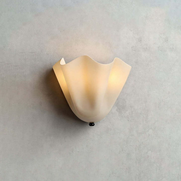 Beige glass wall sconce with black hardware glowing on a pale gray wall.