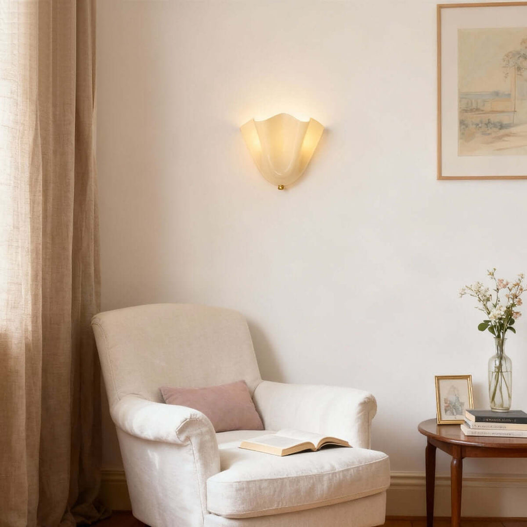 Beige glass wall sconce above a reading chair in a bright sitting area.