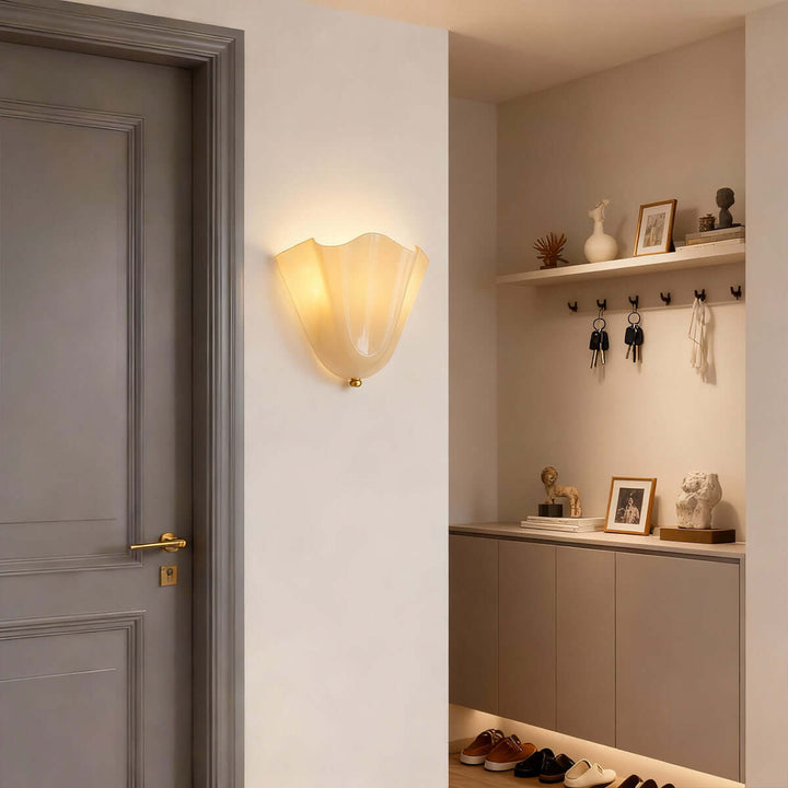 Beige glass wall sconce glowing beside shelves and a doorway.