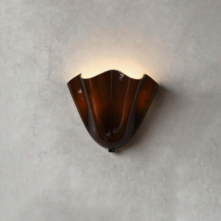Brown glass wall sconce with black hardware glowing on a gray wall.