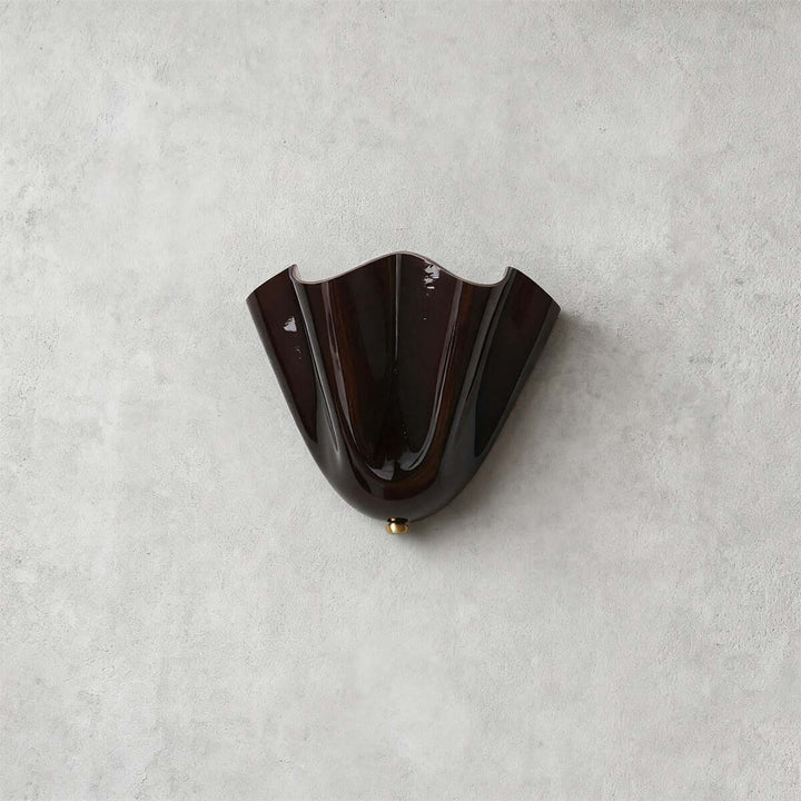 Brown glass wall sconce with gold hardware shown unlit on a gray wall.