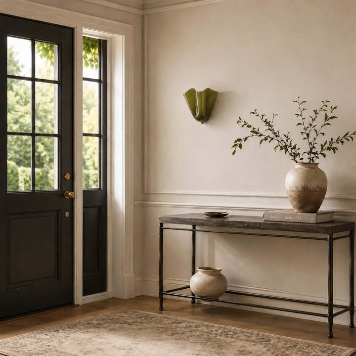Green glass wall sconce mounted above a console near dark entry doors.
