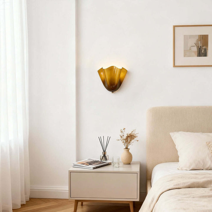 Green glass wall sconce above a nightstand beside a bed.
