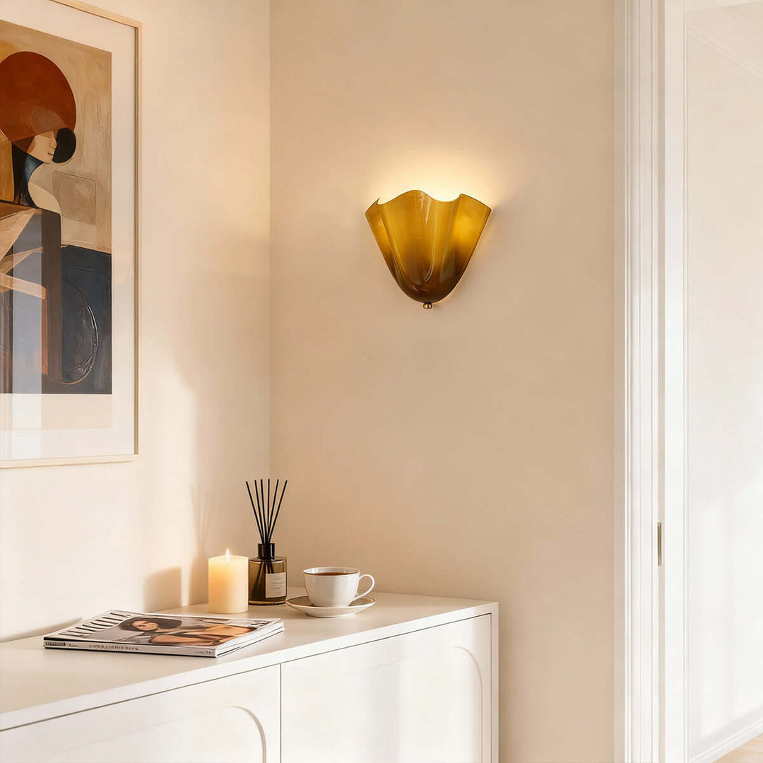 Green glass wall sconce glowing above a dresser with decor and framed art.