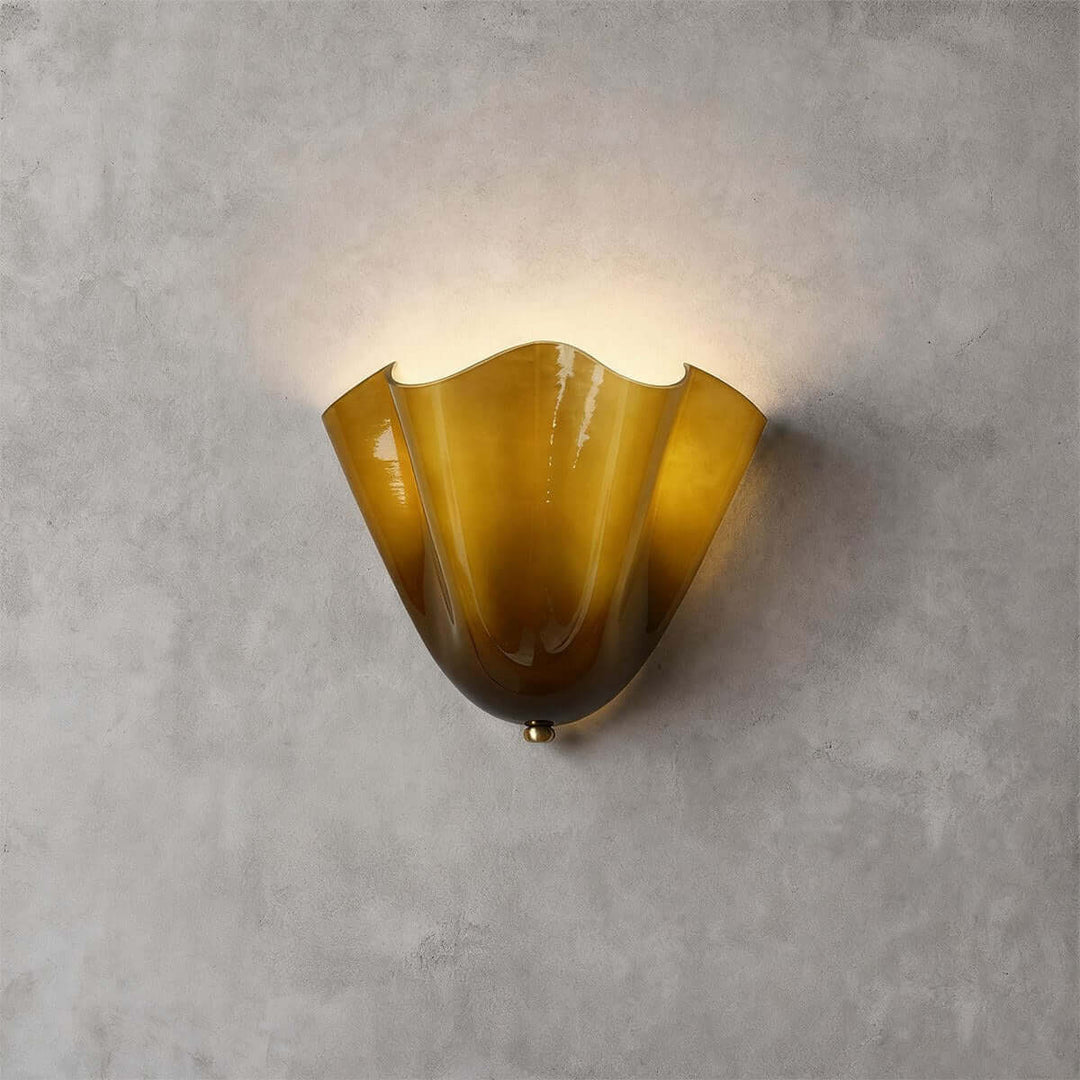 Green glass wall sconce with gold hardware glowing on a gray wall.
