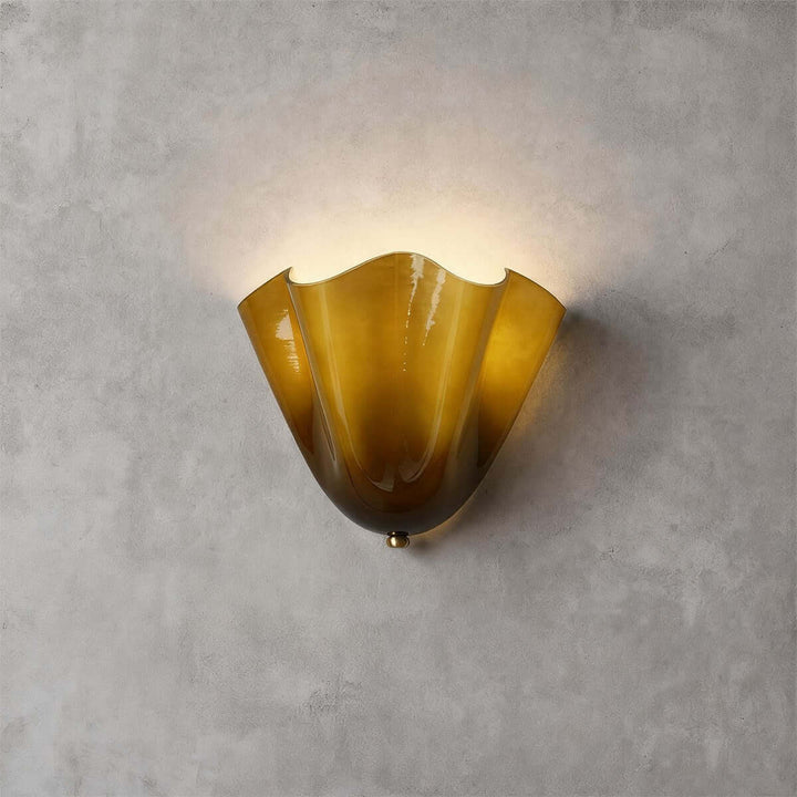 Green glass wall sconce with gold hardware glowing on a gray wall.