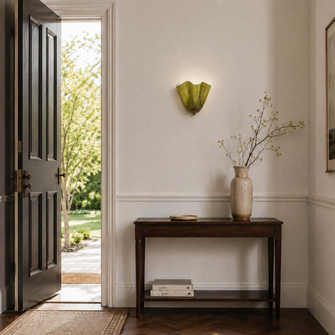 Green glass wall sconce displayed above a slim table near an open doorway.
