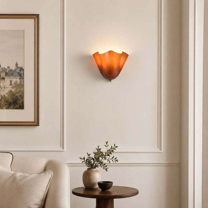 Amber glass wall sconce glowing on a living room wall beside framed art.