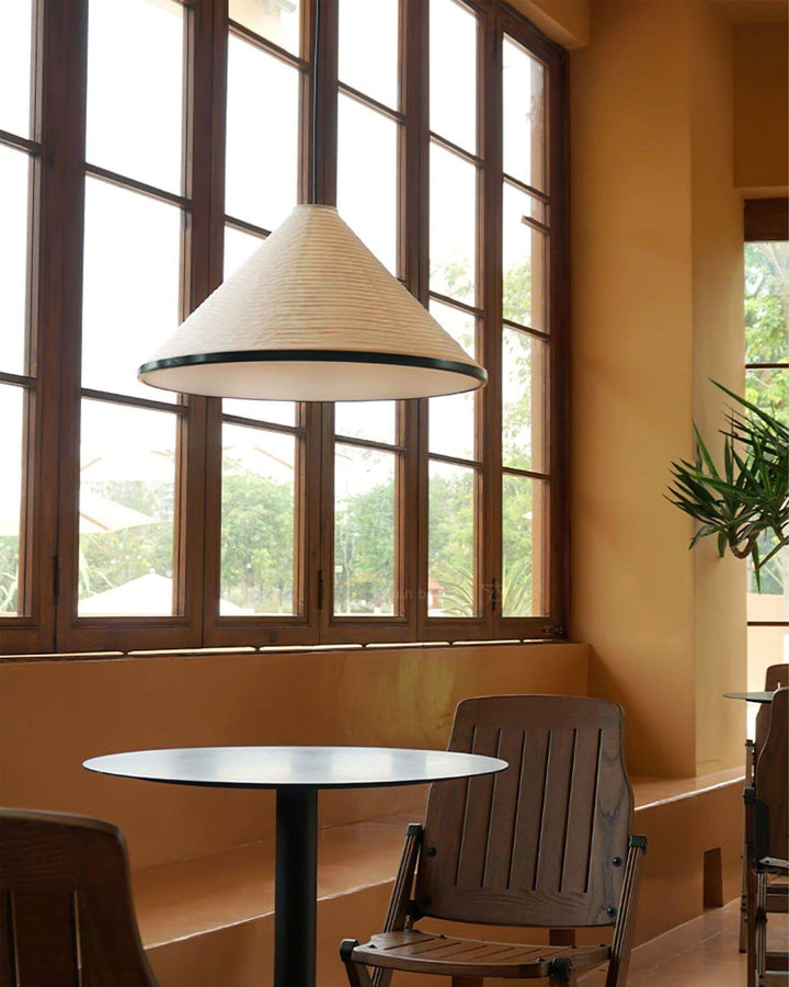 Washi paper cone pendant lamp above a round café table beside a row of tall wood-framed windows