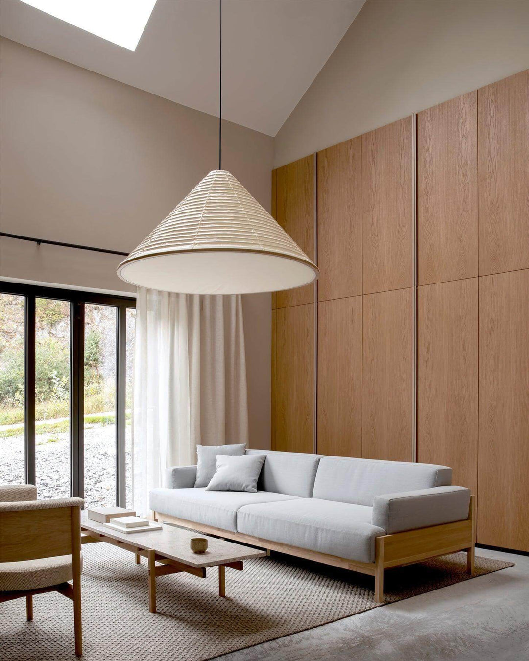 Large Washi paper pendant light with a lower diffuser in a high-ceiling living room with wood walls